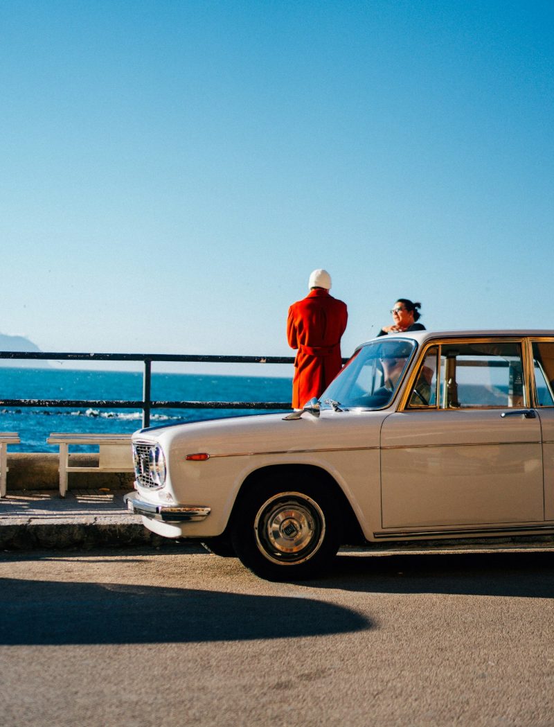 Voiture d’époque garée face à la mer, deux personnes admirant le paysage